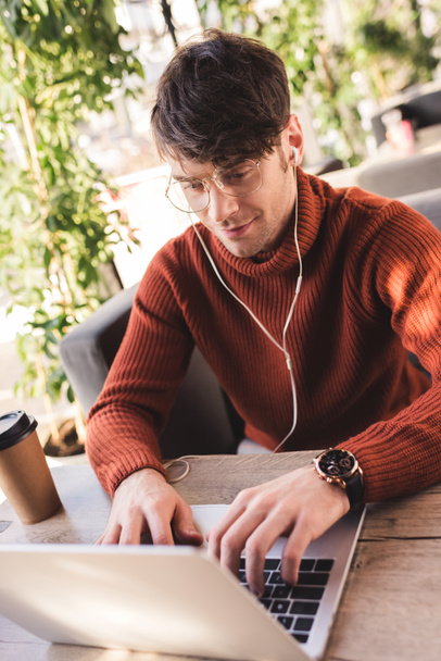 cheerful man listening music in earphones while using laptop in cafe - Photo, Image