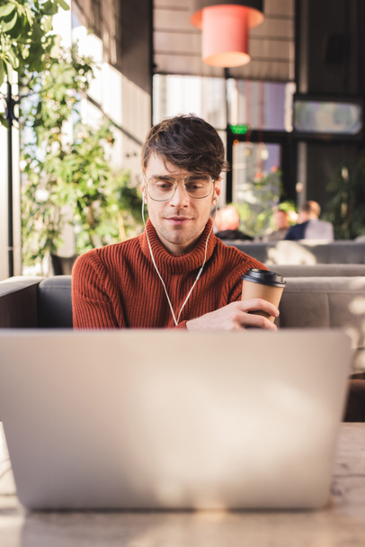 valikoiva painopiste mies kuuntelee musiikkia kuulokkeet käytettäessä kannettavaa tietokonetta ja pitämällä paperimuki kahvilassa
 - Valokuva, kuva