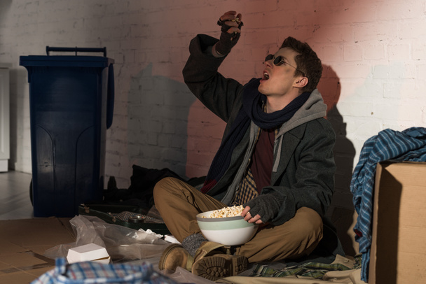 hombre sin hogar comiendo palomitas de maíz mientras está sentado en el basurero
 - Foto, imagen