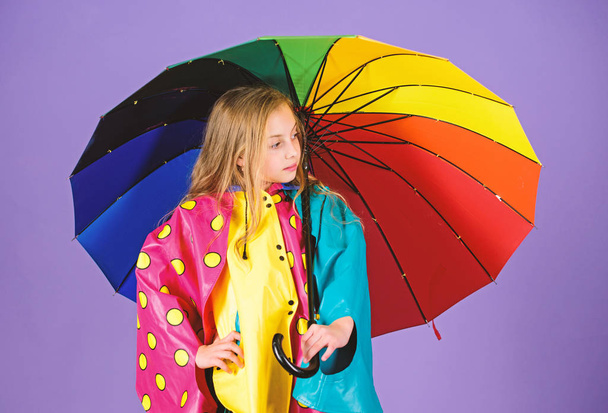 Waterproof accessories for children. Waterproof accessories make rainy day cheerful and pleasant. Kid girl happy hold colorful umbrella wear waterproof cloak. Enjoy rainy weather with proper garments - Foto, Imagen