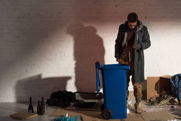 homeless man standing near garbage container surrounded by rubbish - Foto, immagini