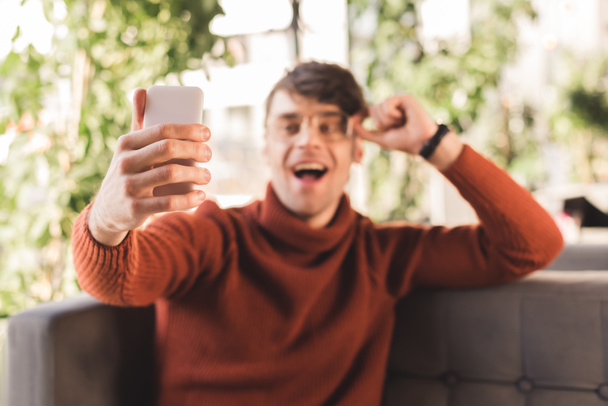 selective focus of cheerful man holding smartphone while taking selfie in cafe - Foto, imagen