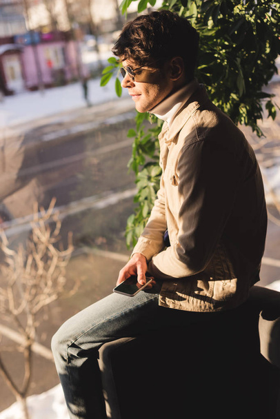 handsome stylish man in sunglasses holding smartphone  - Фото, изображение
