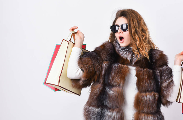 Girl wear sunglasses and fur coat shopping white background. Lady hold shopping bags. Discount and sale. Buy with discount on black friday. Shopping with promo code. Woman shopping luxury boutique - Photo, image
