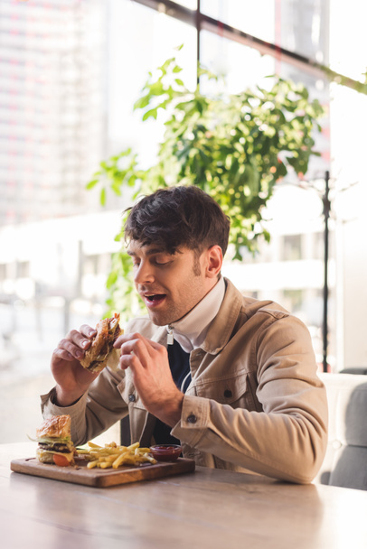 cheerful man eating tasty burger in cafe - Фото, зображення