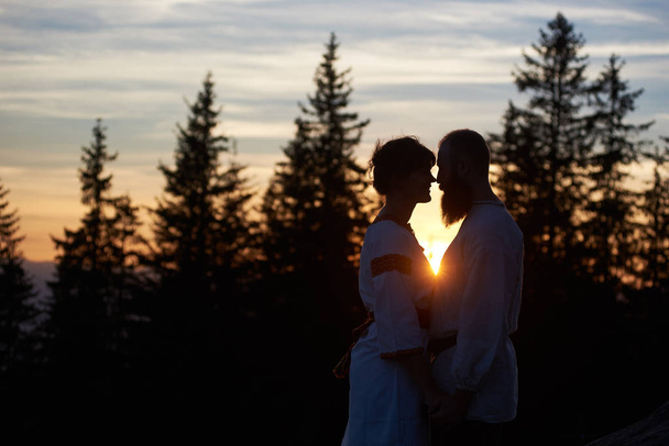 Silhouettes de jeunes couples amoureux debout au sommet de la montagne le soir
 - Photo, image