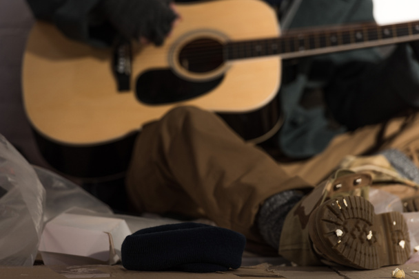selective focus of homeless man playing guitar while sitting on rubbish dump - Fotó, kép