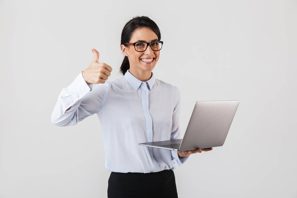 Portrait of attractive businesswoman wearing eyeglasses holding silver laptop in the office isolated over white background - Φωτογραφία, εικόνα