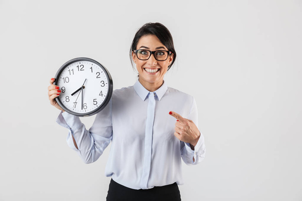 Portrait of smiling businesswoman wearing eyeglasses holding round clock in the office isolated over white background - Fotó, kép
