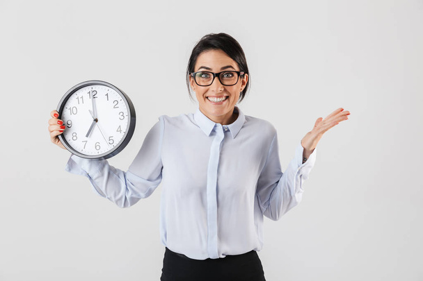 Happy excited businesswoman smartly dressed standing isolated over white background, showing alarm clock - Foto, afbeelding