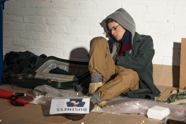 ビジネス新聞はゴミ捨て場に座っているホームレスの男性  - 写真・画像