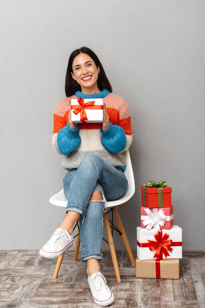 Photo of happy woman 30s sitting in chair with present boxes isolated over gray background - Фото, изображение