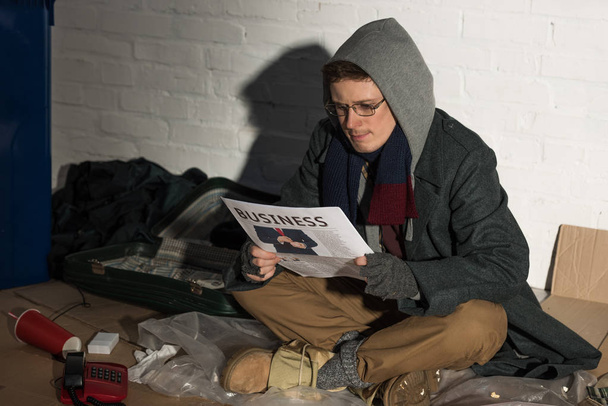 бездомний чоловік читає бізнес-газету, сидячи на сміттєвому звалищі
 - Фото, зображення