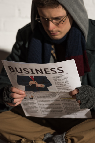 selectieve aandacht van dakloze man in glazen en kap business krant lezen - Foto, afbeelding