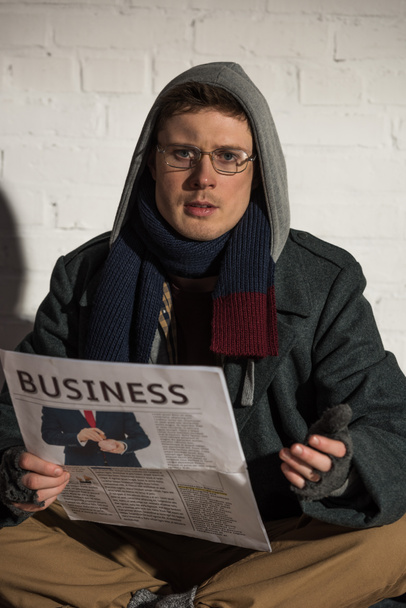 бездомний чоловік читає бізнес-газету і дивиться на камеру
 - Фото, зображення