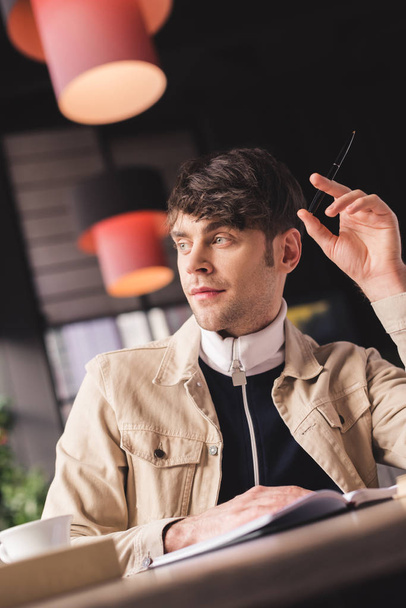 вибірковий фокус людини, що сидить в кафе і тримає ручку в руці в кафе
 - Фото, зображення