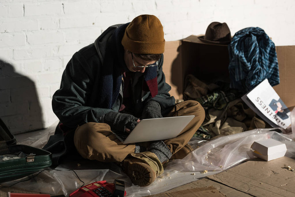 homeless man in glasses and fingerless gloves using laptop - 写真・画像
