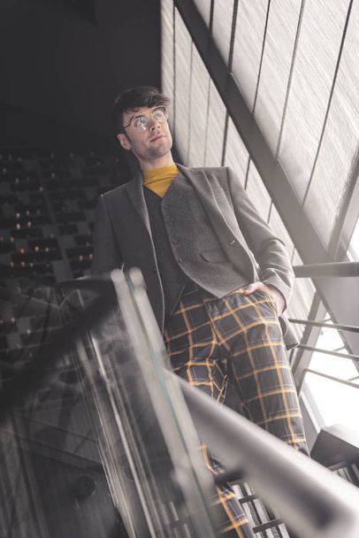 cheerful stylish man in glasses standing with hand in pocket on stairs - Photo, Image