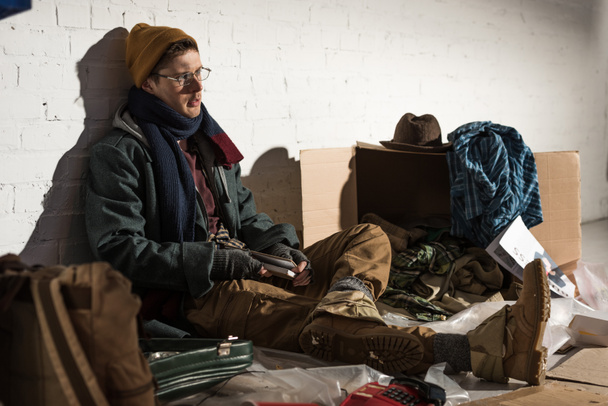 ゴミに囲まれたレンガの壁に腰掛けていたホームレスの男 - 写真・画像