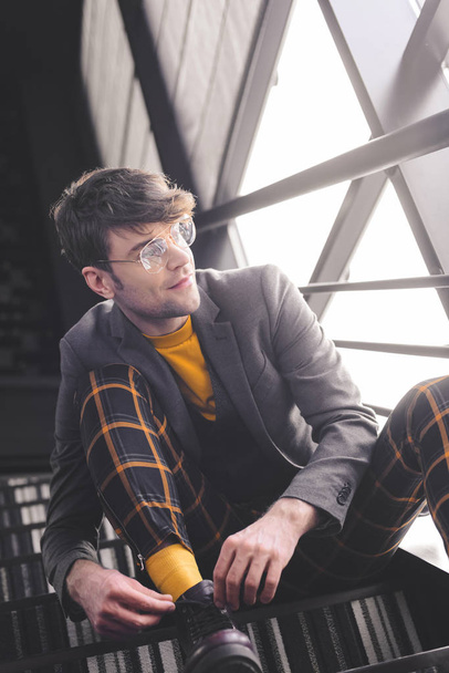 happy stylish man in glasses sitting on stairs near windows - Фото, зображення