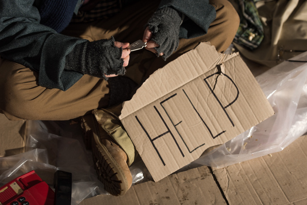 cropped view of homeless man sitting with cardboard card with "help" handwritten text - Фото, изображение