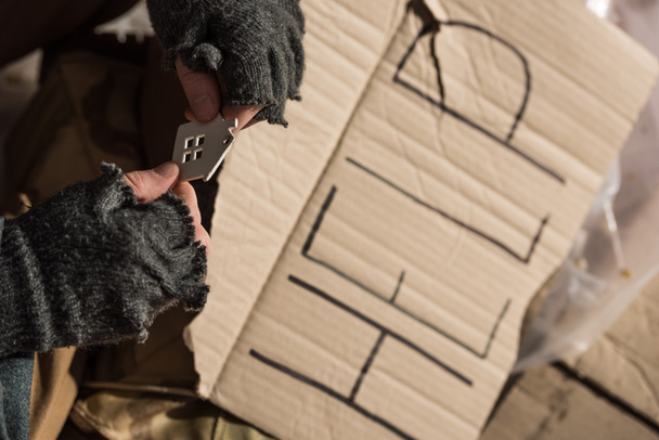 vue recadrée d'un sans-abri assis avec une carte en carton avec du texte manuscrit "à l'aide" et tenant une maison coupée en papier
 - Photo, image
