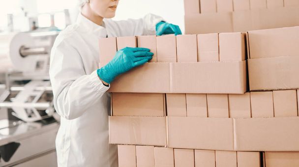 junge Mitarbeiterin in sterilen Uniformanzählboxen während sie in der Lebensmittelfabrik steht. - Foto, Bild