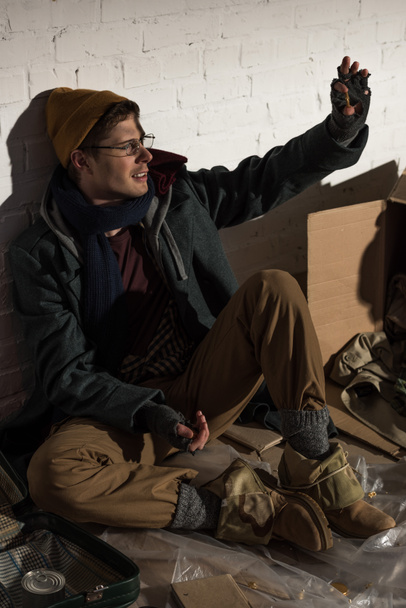 mendigo sin hogar hombre sentado por la pared de ladrillo y saludando de la mano
 - Foto, Imagen