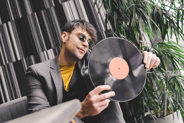 stylish young man in sunglasses looking at vinyl record  - Фото, зображення