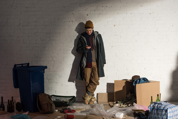 dakloze man met behulp van smartphone terwijl staande op vuilnisbelt - Foto, afbeelding