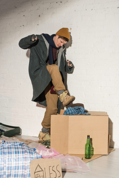 hombre sin hogar agresivamente empujando basura en la caja pateando
 - Foto, Imagen