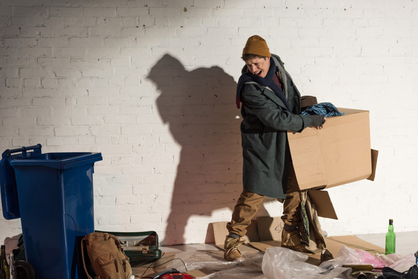 злий бездомний чоловік тримає картонну коробку зі сміттям
 - Фото, зображення