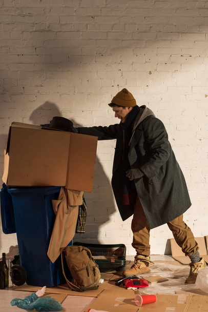 homeless begar man pushing cardboard box with rubbish into trash container - Foto, Imagem