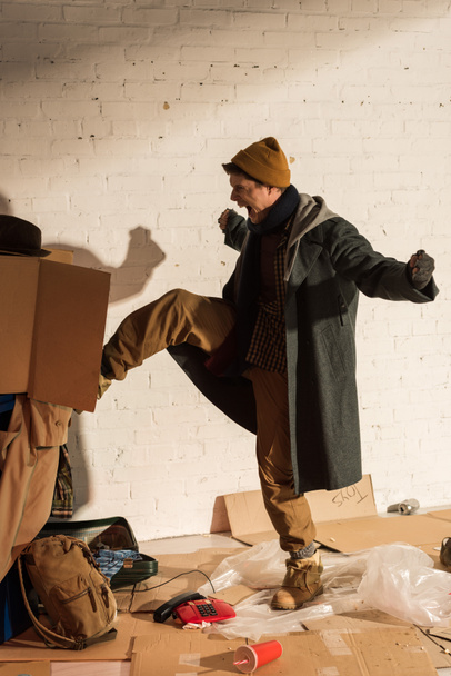 agressief schreeuwen dakloze man schoppen prullenbak container met kartonnen doos - Foto, afbeelding