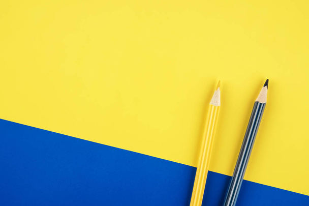 blaue und gelbe Buntstifte auf farbigem Papier Hintergrund. minimalistisches, kreatives Konzept - Foto, Bild