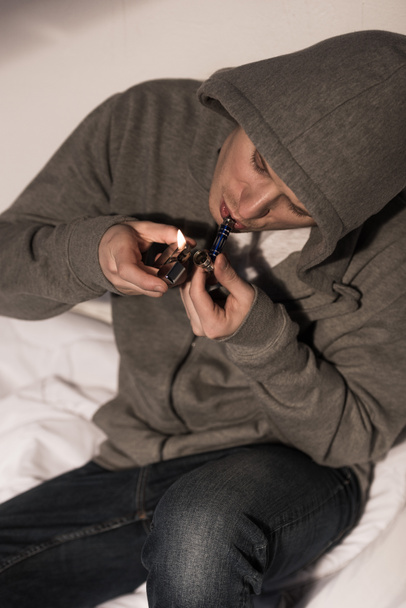 selective focus of addicted man lightening smoking pipe with metallic lighter  - Foto, Imagem