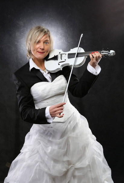 symbióza nevěsty a ženicha, emocionální smyslnost blondýna v svatební šaty a oblek, drží bílé housle - Fotografie, Obrázek
