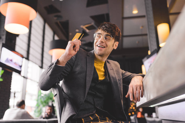 Glimlachende man in glazen terwijl creditcard in café de toog achter - Foto, afbeelding