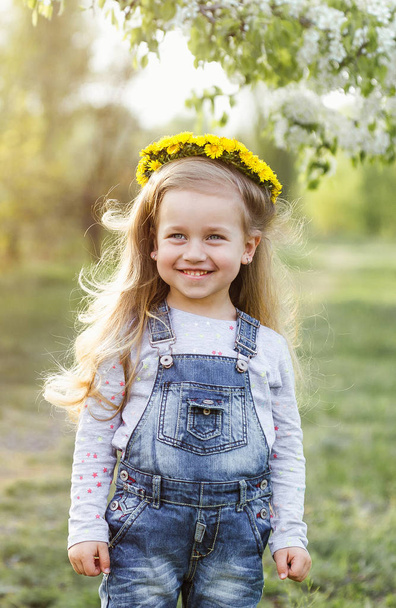 Spring sunny portrait of a cute 4 year old girl posing with a dandelion wreath, looking at the camera - Foto, afbeelding