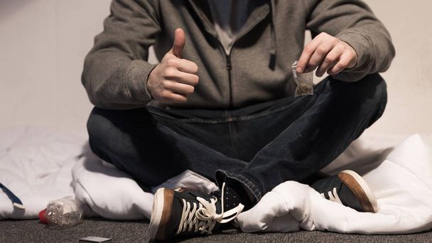 selective focus of addictive man holding pack of marijuana and showing thumb up - Фото, зображення