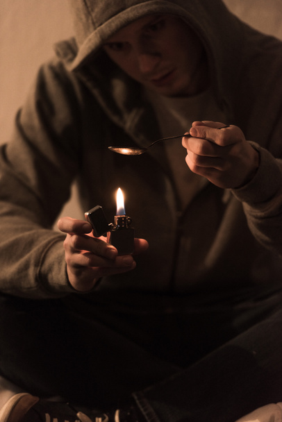 selective focus of addict man boiling heroin in spoon on lighter - 写真・画像