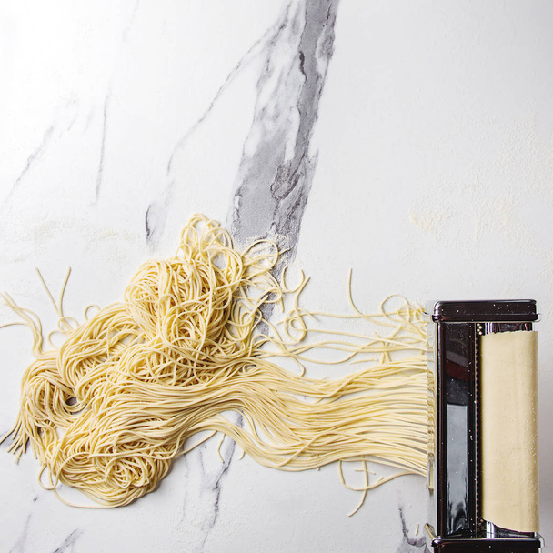 Rolled dough for homemade italian uncooked pasta spaghetti from pasta machine maker with semolina flour over white marble texture background. Flat lay, space. Square image - Fotografie, Obrázek