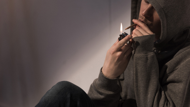 addict man in hood lightening rolled marijuana cigarette - Photo, Image