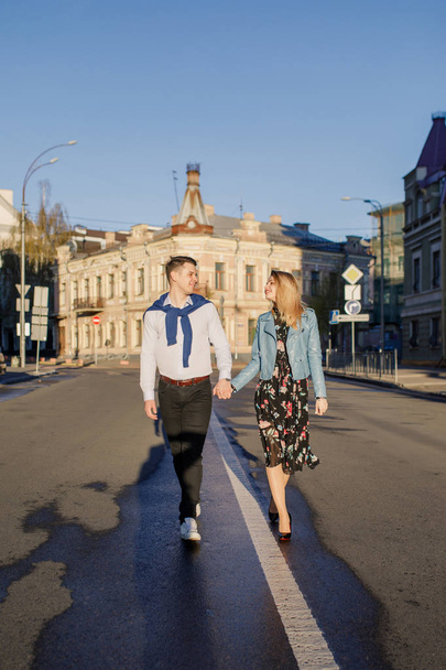 young stylish couple walking on sun lighted street holding hands - Photo, image