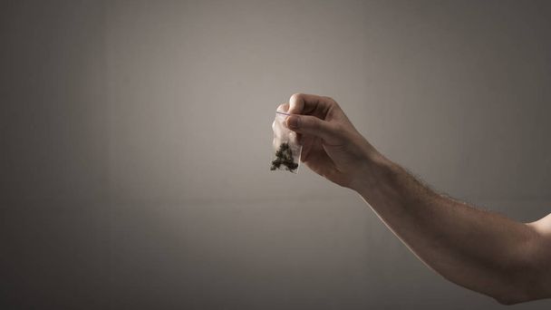 vista parcial del hombre sosteniendo el paquete con marihuana sobre fondo gris
 - Foto, Imagen