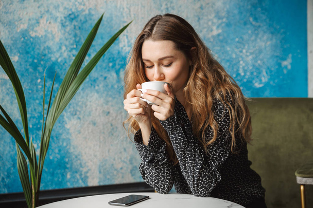 Foto von schönen jungen hübschen Frau sitzt im Café drinnen Kaffee trinken. - Foto, Bild