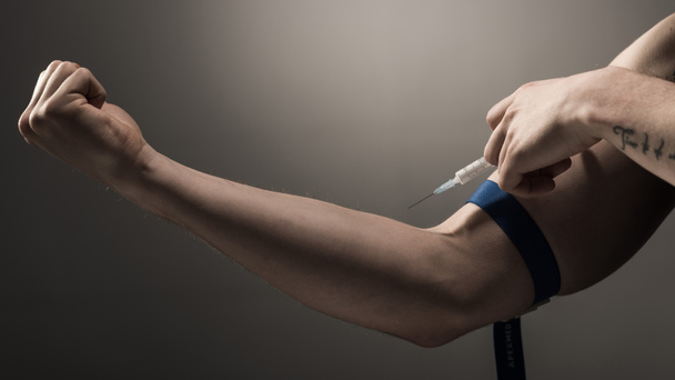 gedeeltelijke weergave van verslaafde man maken van injectie van heroïne dosis op grijze achtergrond  - Foto, afbeelding