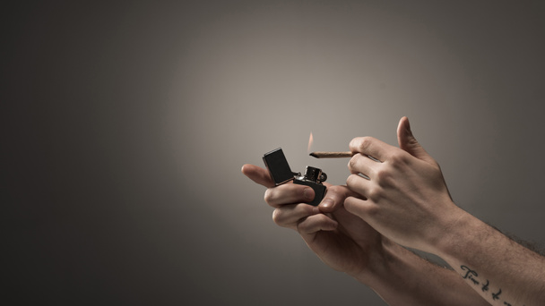 vista parcial del aligeramiento masculino cigarrillo de marihuana enrollado sobre fondo gris
 - Foto, Imagen