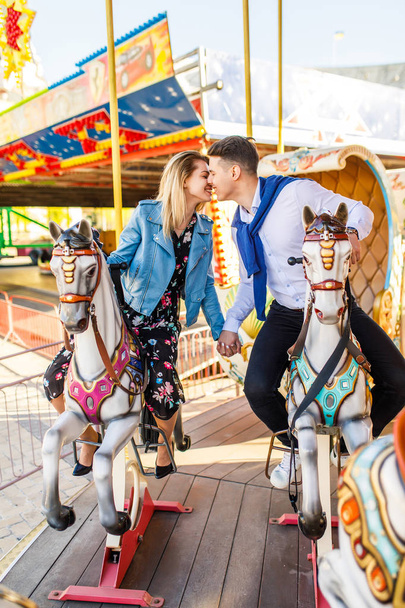 young couple sitting on carousel horses and kissing - Foto, afbeelding