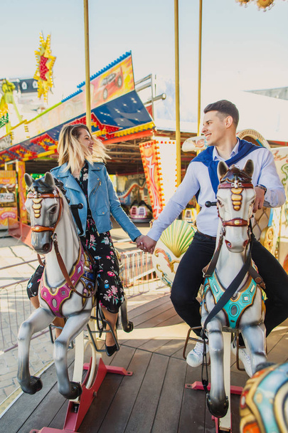 young couple sitting on carousel horses and holding hands - Foto, Imagem